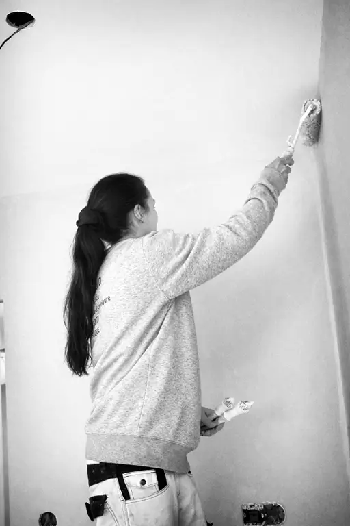 Matériel peinture professionnel pour travaux intérieurs en hiver – Malige Peintre professionnel appliquant de la peinture blanche au rouleau sur un mur intérieur, avec rouleaux, pinceaux et outils de préparation de chantier au premier plan.